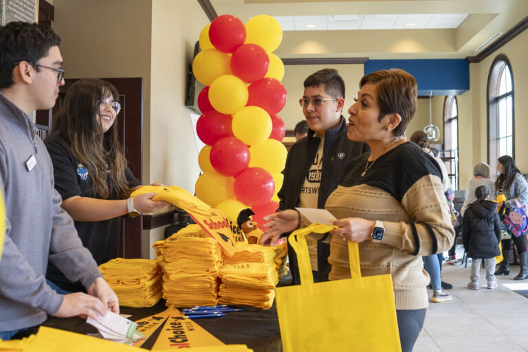 A parent and her son receive a scarf and pennant from workers at a table