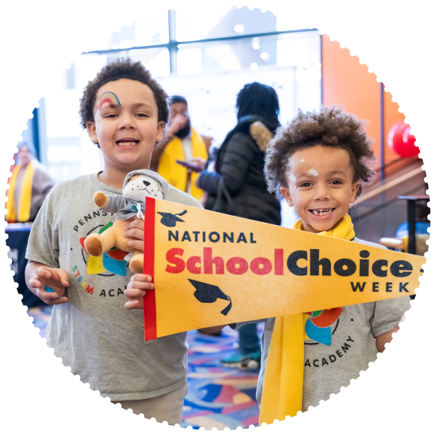 Two students smile for the camera, holding up a School Choice week pennant