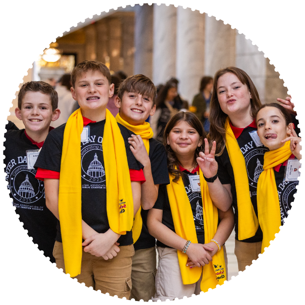 A group of students wearing scarves smile and pose for a photo at a capitol event