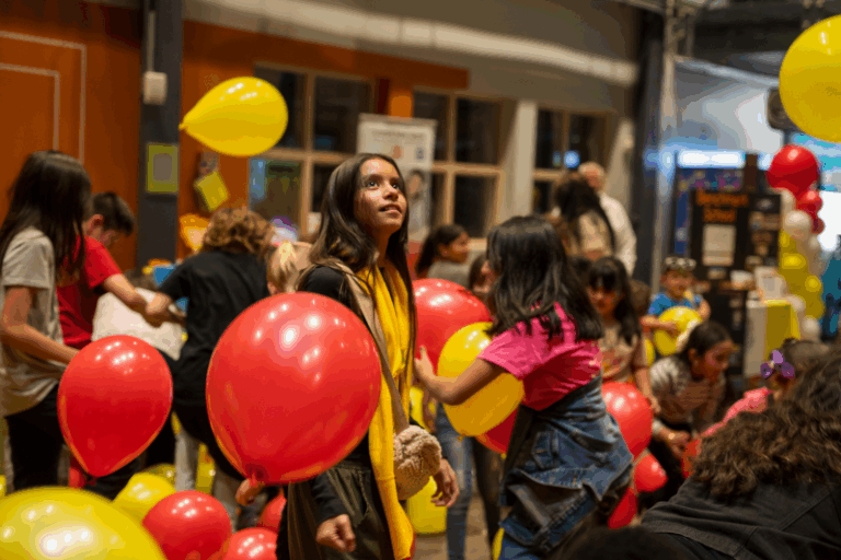 A girl looks up as balloons drop from the ceiling at a school fair